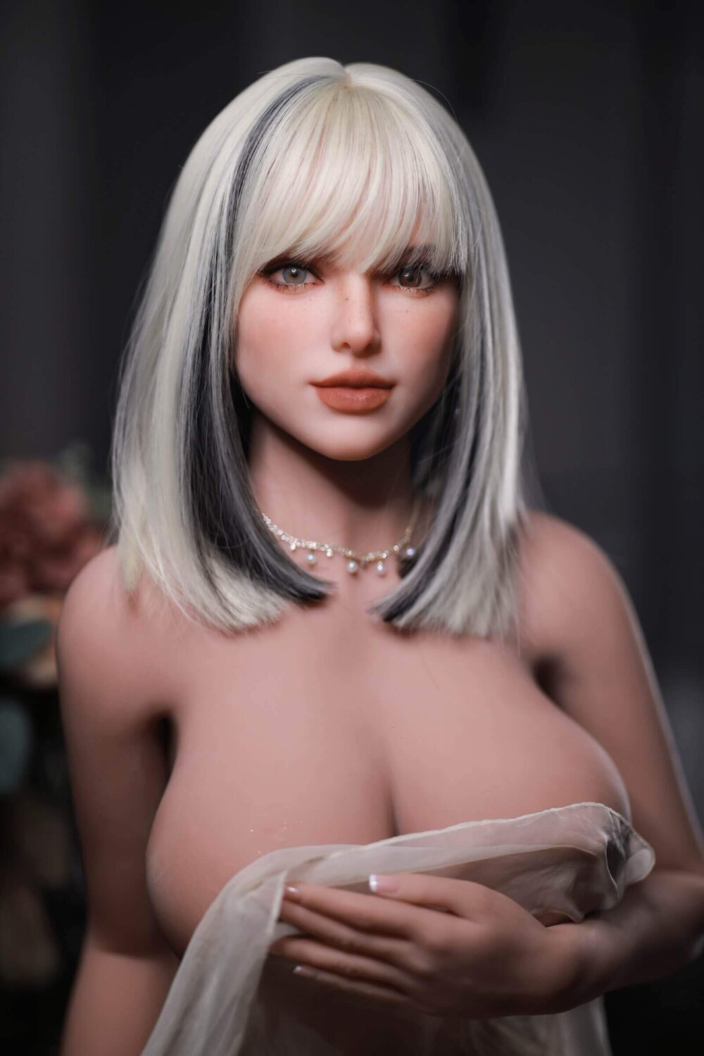 SexDoll kurzes blondes Haar mit schwarzen Akzenten, zwei verschiedenfarbige Augen, große Lippen, große Brüste mit Stoff bedeckt, silberne Halskette